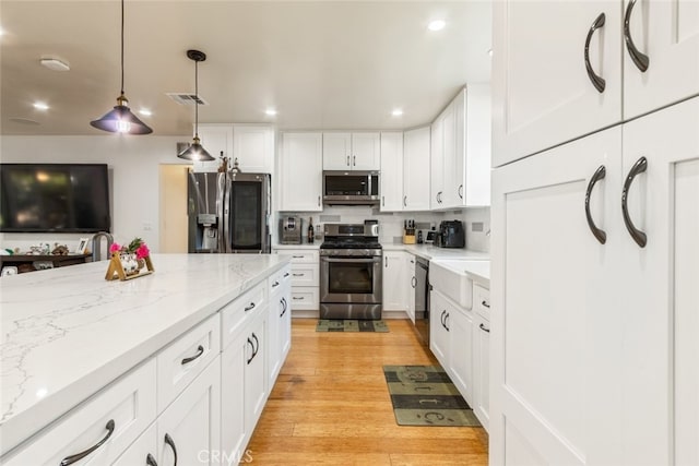 kitchen with light stone counters, tasteful backsplash, stainless steel appliances, light wood finished floors, and hanging light fixtures