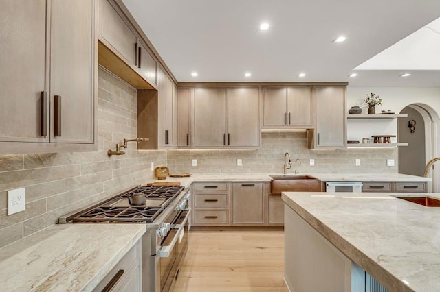 kitchen featuring light wood-type flooring, open shelves, a sink, arched walkways, and range with two ovens