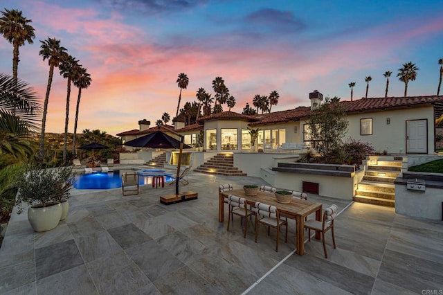 patio terrace at dusk featuring outdoor dining area, an outdoor pool, and a hot tub