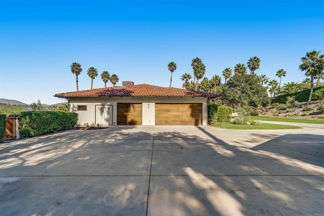 mediterranean / spanish house with stucco siding, driveway, a tile roof, a garage, and a chimney