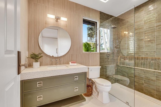 bathroom with tile patterned flooring, toilet, vanity, a tile shower, and tile walls