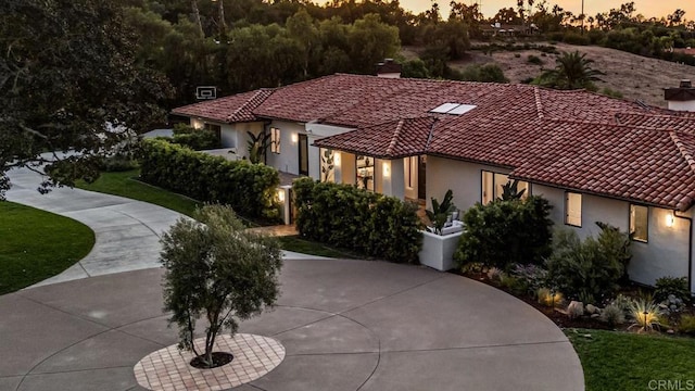 view of front of home featuring stucco siding, driveway, a chimney, and a tiled roof