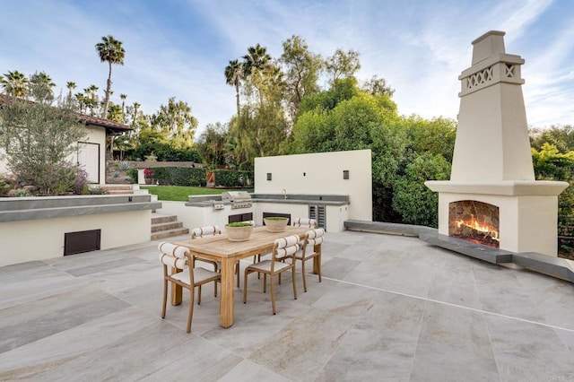 view of patio / terrace with a sink, grilling area, a lit fireplace, outdoor dining area, and an outdoor kitchen