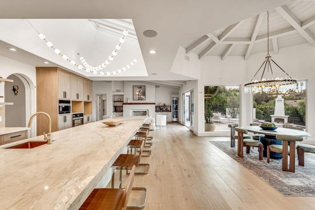 kitchen featuring beam ceiling, oven, a sink, a notable chandelier, and light wood-type flooring