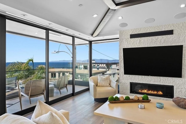 living area with lofted ceiling with beams, expansive windows, a fireplace, and wood finished floors