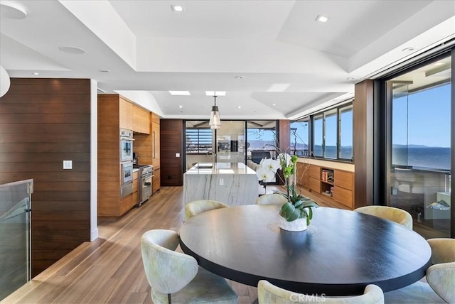 dining space featuring wood walls, recessed lighting, a raised ceiling, and light wood-style floors