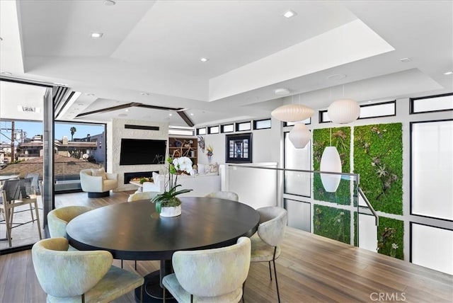 dining room featuring a large fireplace, a raised ceiling, and wood finished floors