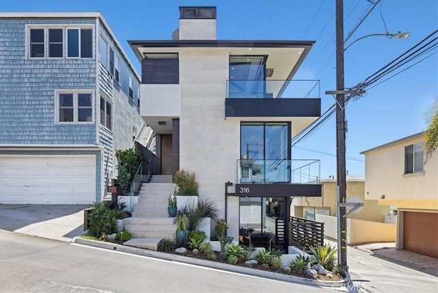 modern home with a garage, stairs, a chimney, and concrete driveway