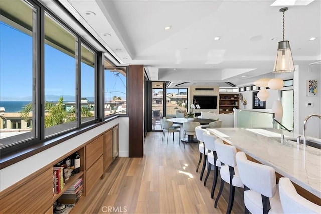 kitchen with a breakfast bar, light wood-type flooring, light stone countertops, a tray ceiling, and decorative light fixtures