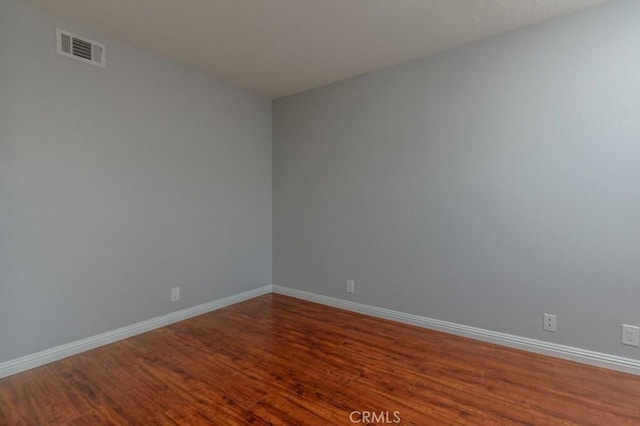 empty room with dark wood-type flooring, visible vents, and baseboards