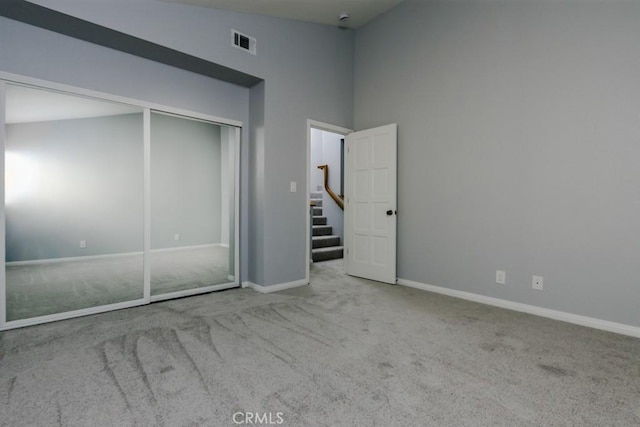 unfurnished bedroom featuring baseboards, visible vents, a high ceiling, carpet flooring, and a closet