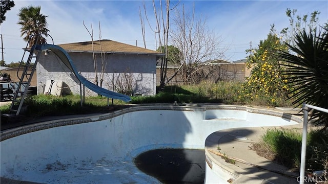 exterior space featuring a water slide, fence, and an empty pool