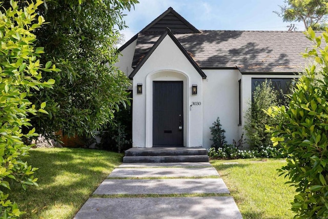 view of front of property featuring a front lawn, roof with shingles, and stucco siding