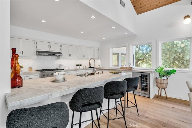 kitchen featuring visible vents, backsplash, a sink, beverage cooler, and under cabinet range hood