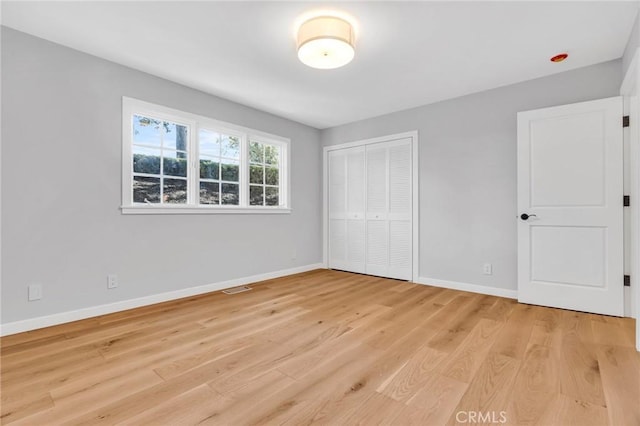 unfurnished bedroom with a closet, visible vents, light wood finished floors, and baseboards