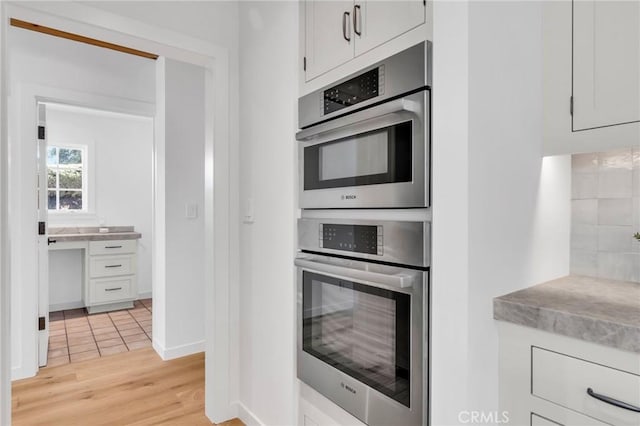 kitchen with stainless steel double oven, light countertops, light wood-style flooring, and white cabinetry