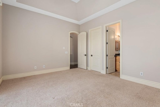 unfurnished bedroom with arched walkways, carpet flooring, ensuite bath, and baseboards