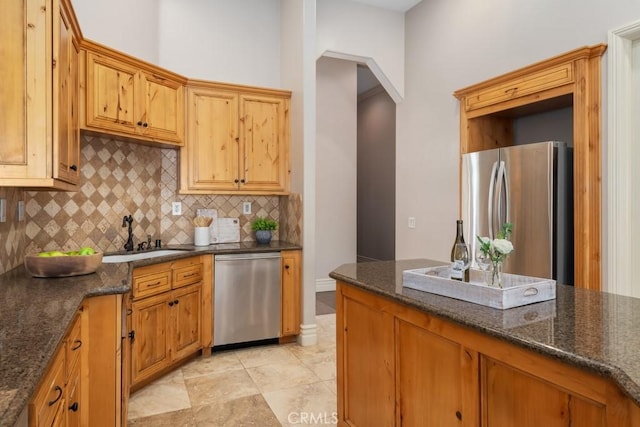 kitchen with appliances with stainless steel finishes, dark stone counters, a sink, and backsplash