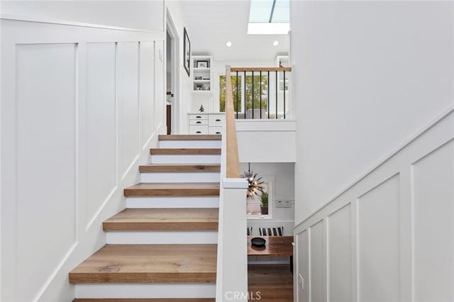 staircase with recessed lighting, a skylight, a towering ceiling, and a decorative wall