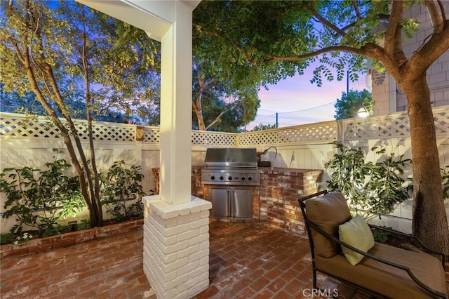 patio terrace at dusk featuring exterior kitchen, a fenced backyard, and grilling area