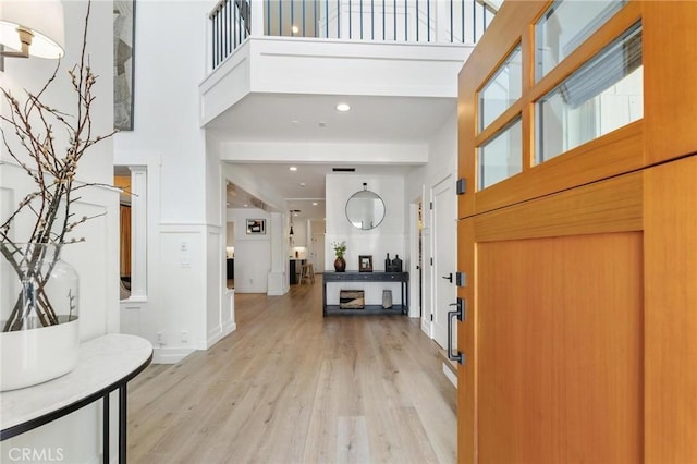 foyer featuring a wainscoted wall, light wood finished floors, a high ceiling, and a decorative wall