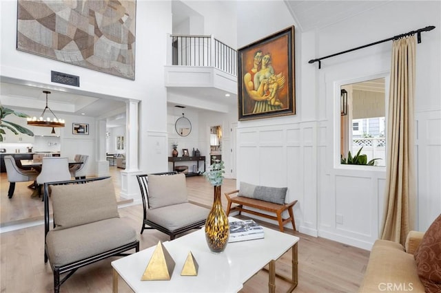 living area featuring a notable chandelier, a decorative wall, light wood finished floors, and ornate columns