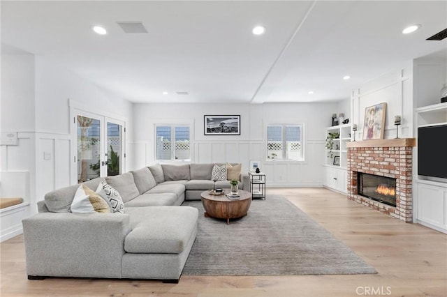 living area with light wood-style floors, recessed lighting, a brick fireplace, and french doors