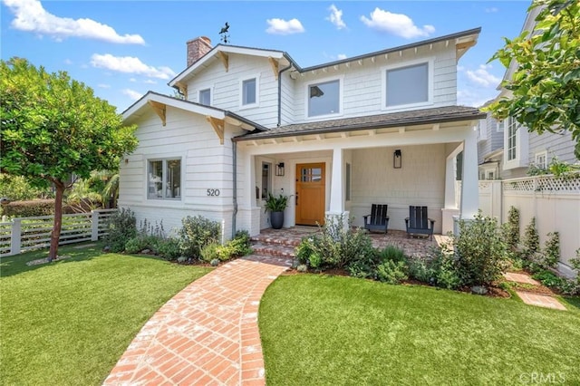 view of front of property featuring covered porch, a chimney, fence, and a front lawn