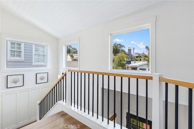 interior space with a decorative wall, wood finished floors, an upstairs landing, vaulted ceiling, and wainscoting