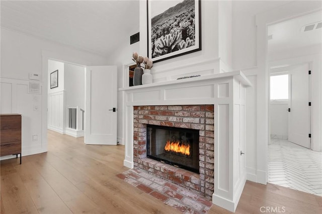 living area featuring visible vents, wood finished floors, vaulted ceiling, a brick fireplace, and a decorative wall