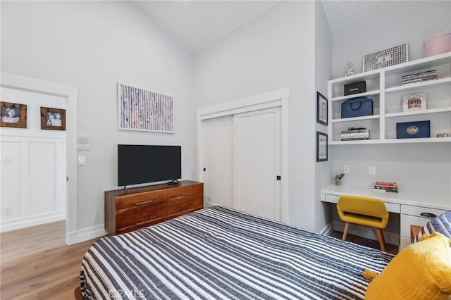 bedroom featuring baseboards, vaulted ceiling, light wood-style floors, built in desk, and a closet