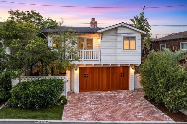 view of front of home featuring a balcony, a garage, a chimney, and decorative driveway