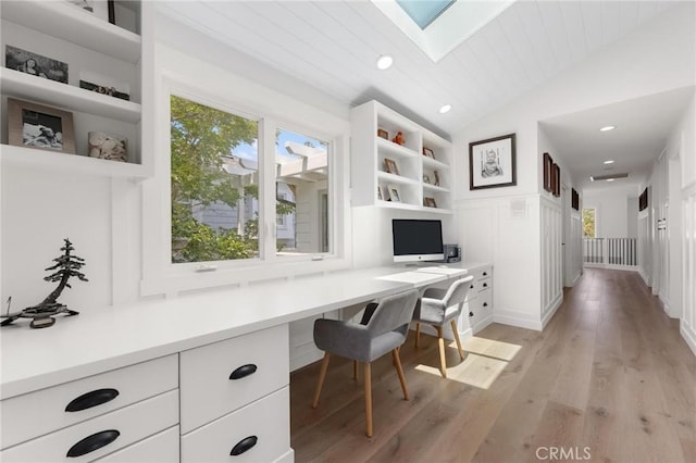 office with lofted ceiling with skylight, recessed lighting, built in desk, and light wood finished floors