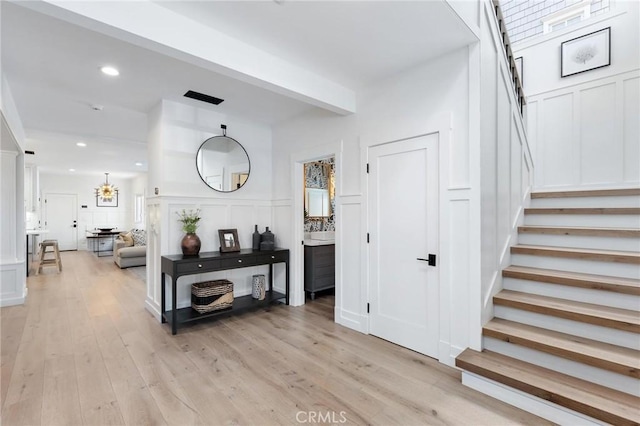 interior space featuring light wood-type flooring, stairs, a decorative wall, and beam ceiling