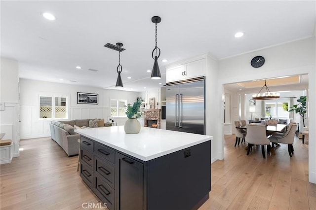 kitchen featuring light wood-style flooring, a kitchen island, decorative light fixtures, and built in fridge