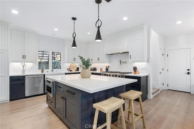 kitchen featuring premium range hood, white cabinets, a kitchen breakfast bar, light countertops, and appliances with stainless steel finishes