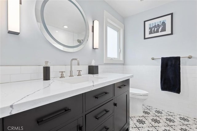 bathroom featuring toilet, a wainscoted wall, tile walls, and vanity