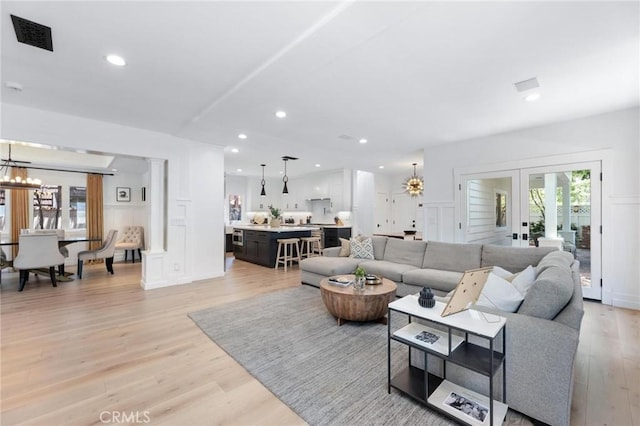 living area with a chandelier, french doors, light wood-style flooring, and a decorative wall