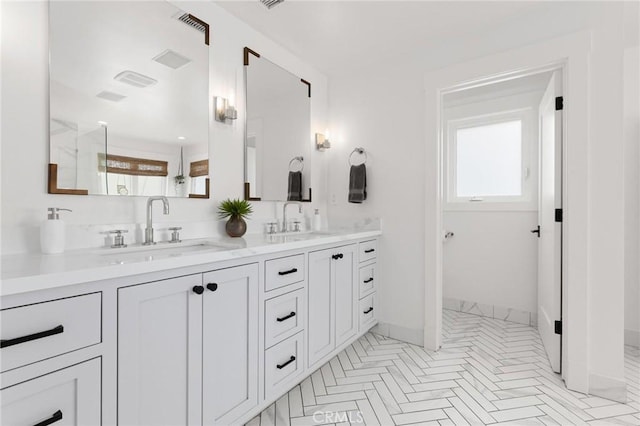 full bathroom with double vanity, a sink, a shower with door, and baseboards