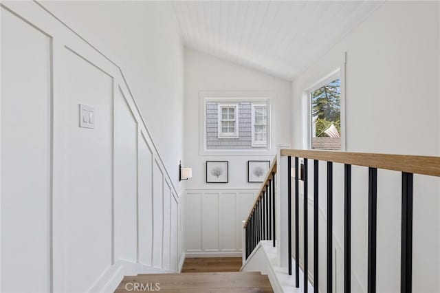 staircase featuring a decorative wall, vaulted ceiling, wood finished floors, and wainscoting