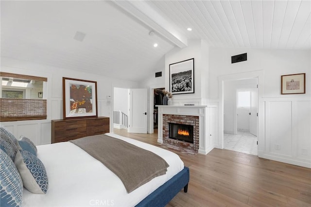 bedroom featuring lofted ceiling with beams, a decorative wall, a fireplace, visible vents, and light wood finished floors