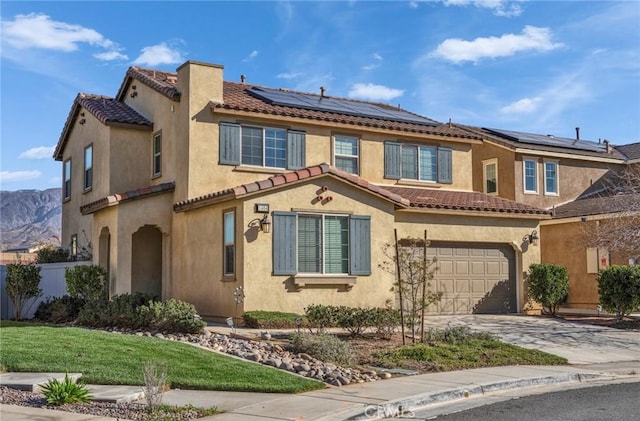 mediterranean / spanish-style home with driveway, an attached garage, fence, roof mounted solar panels, and stucco siding