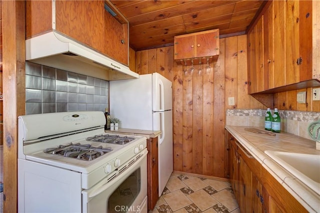 kitchen featuring under cabinet range hood, gas range gas stove, backsplash, and tile countertops