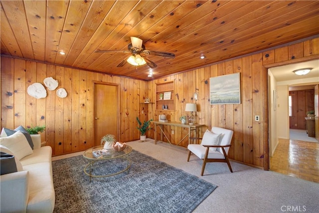 living area featuring a ceiling fan, carpet, wooden ceiling, and wooden walls