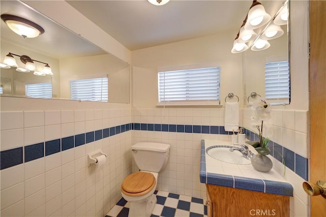 half bath featuring tile patterned floors, tile walls, toilet, and vanity