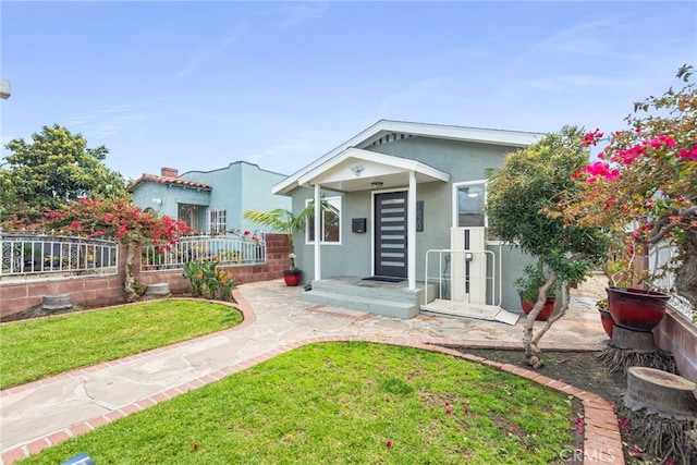 view of front of house featuring stucco siding, a front lawn, and fence