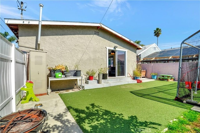 rear view of property featuring a fire pit, fence, a patio, and stucco siding