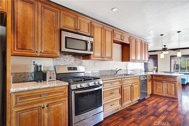 kitchen with brown cabinets, dark wood-type flooring, a peninsula, stainless steel appliances, and a sink