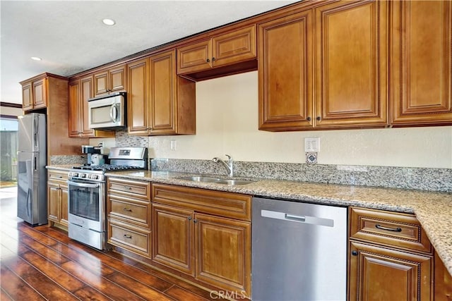 kitchen with stainless steel appliances, brown cabinetry, a sink, and dark wood-type flooring