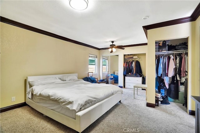 carpeted bedroom featuring baseboards, ceiling fan, two closets, and crown molding